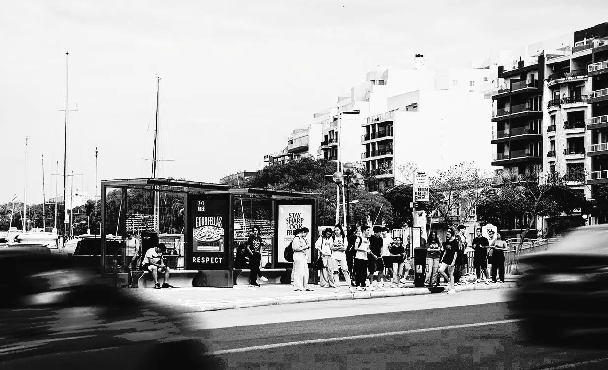 FACES bus shelter on the Sliema promenade with a queue of waiting passengers