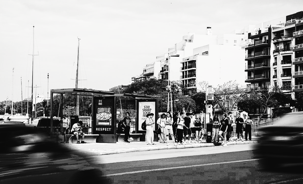FACES bus shelter on the Sliema promenade with a queue of waiting passengers